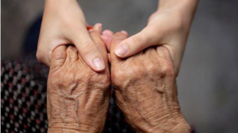 younger hands holding hands of elderly